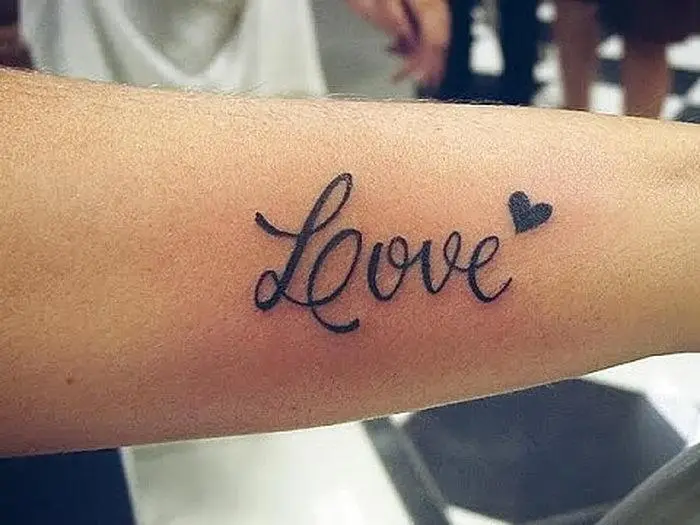 Tattoo with the inscription love with a heart closer to the elbow